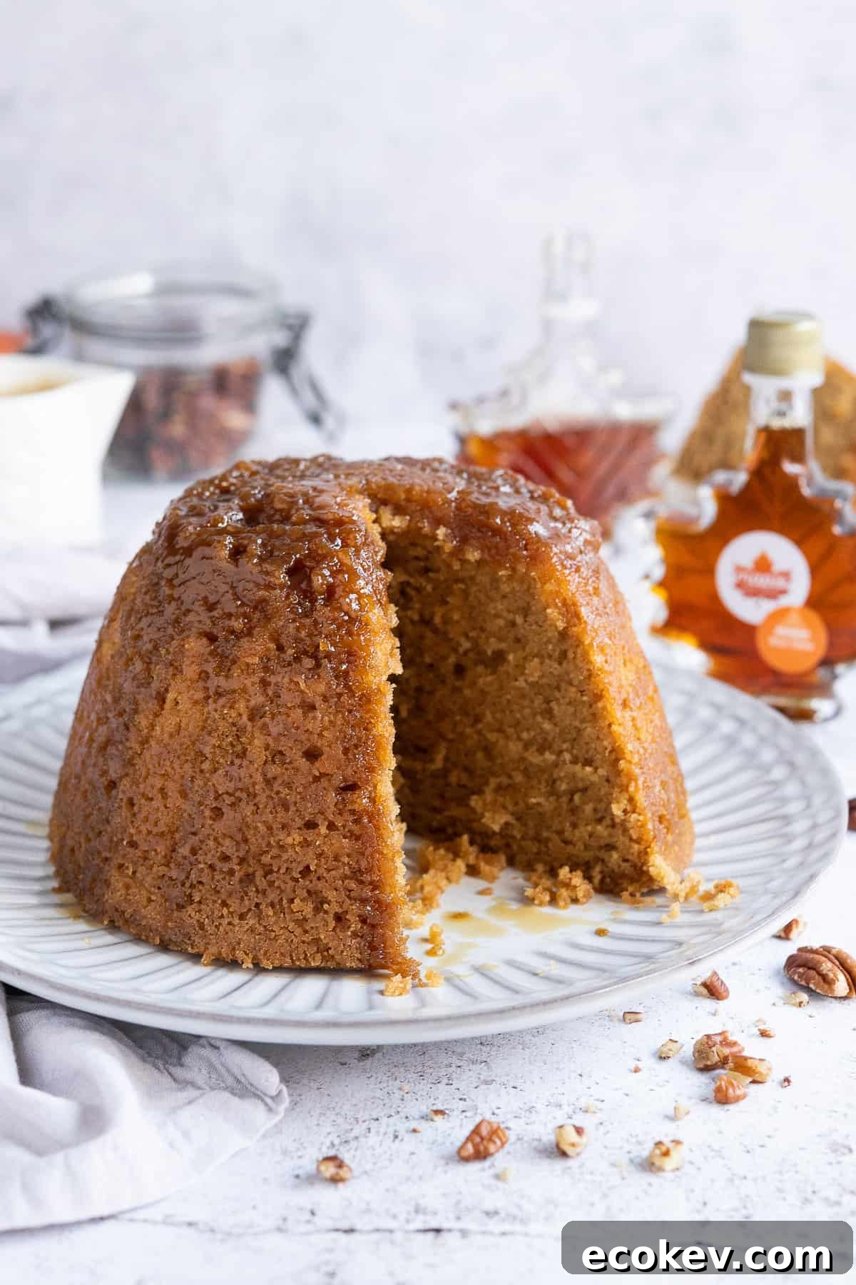 Steamed maple syrup pudding on a white plate with a slice removed.