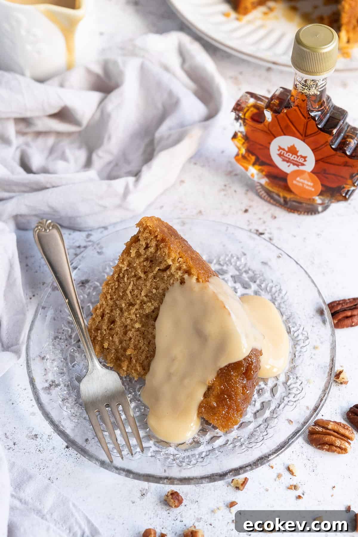 A slice of steamed maple syrup pudding topped with maple custard on a glass plate with a fork.