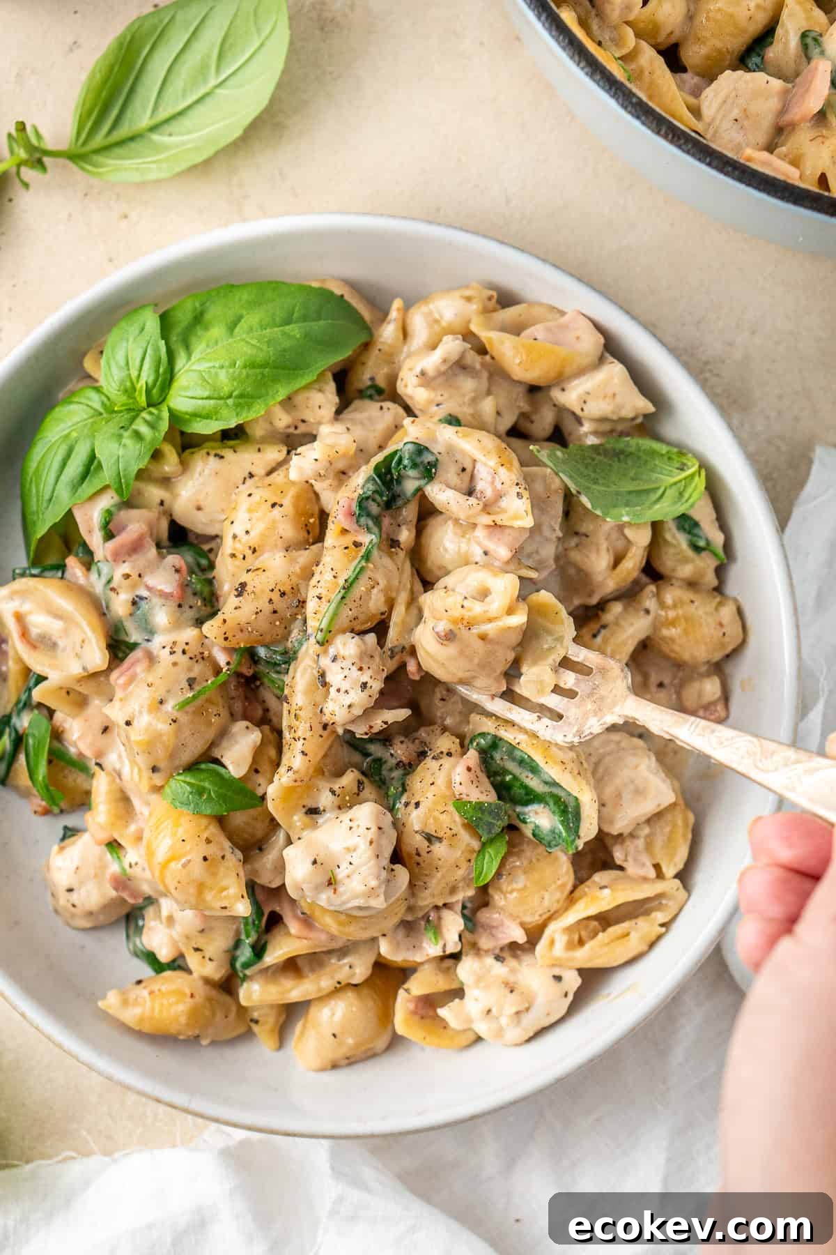 Close up of a fork taking a bite of creamy chicken and bacon pasta.