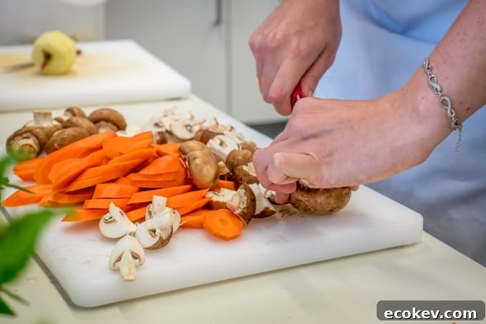 Female hands chopping carrots and mushrooms on white cut board.