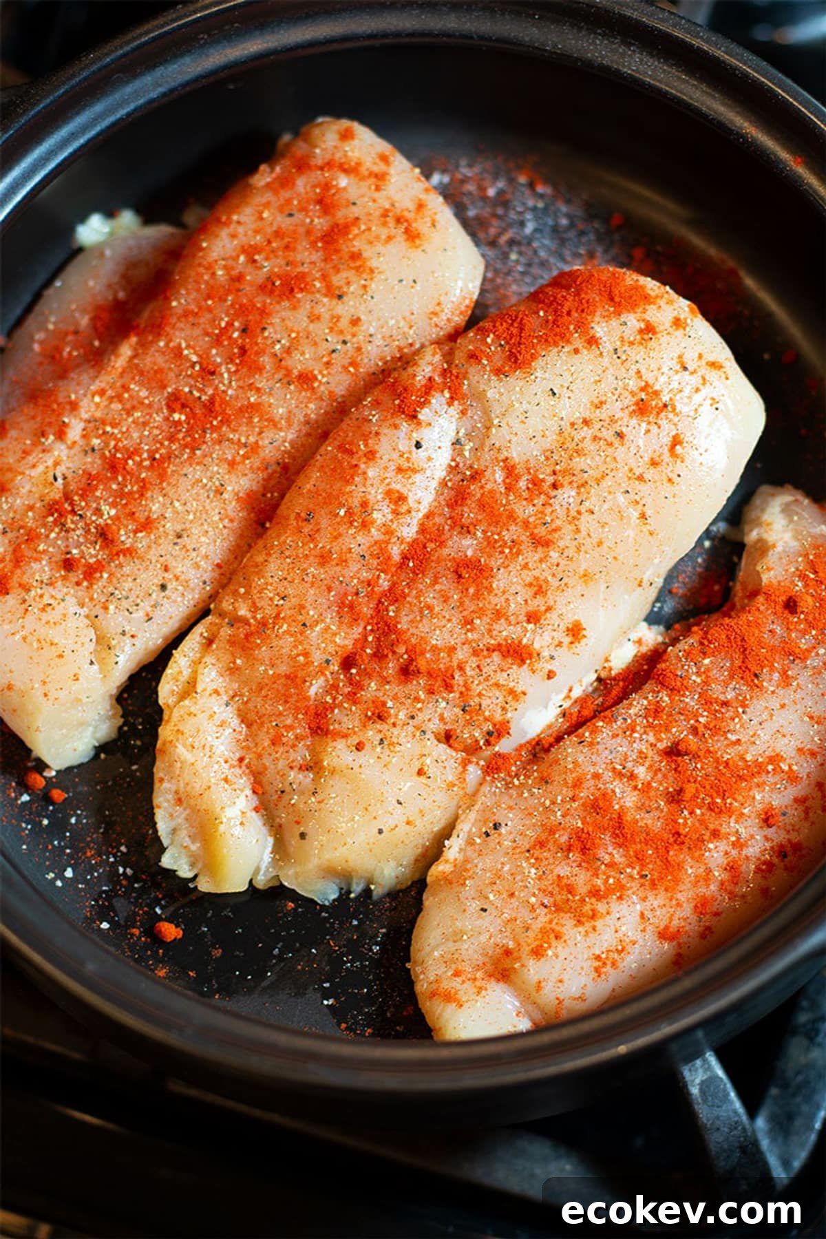 Three chicken breasts sprinkled with smoked Paprika, salt and pepper in a black pan.