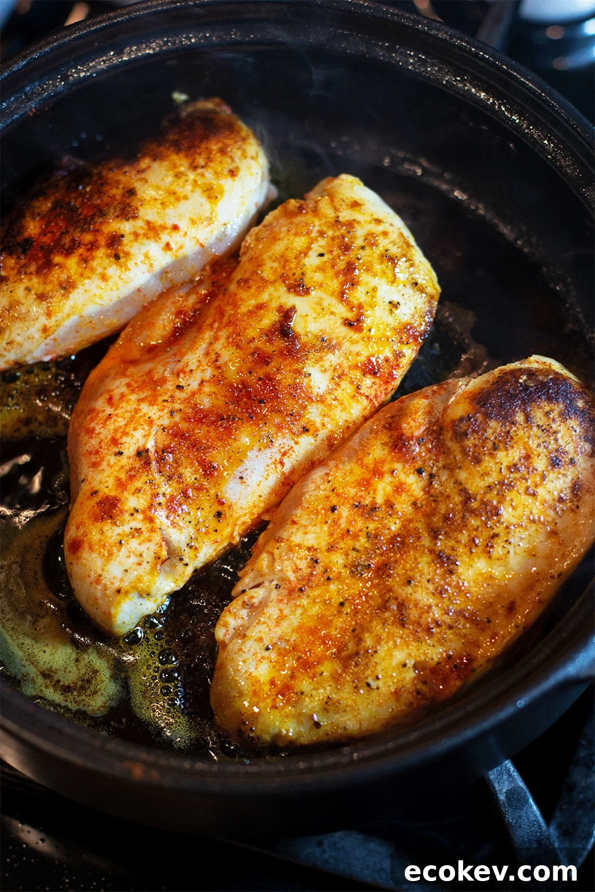 Three sauteed chicken breasts in a black pan.