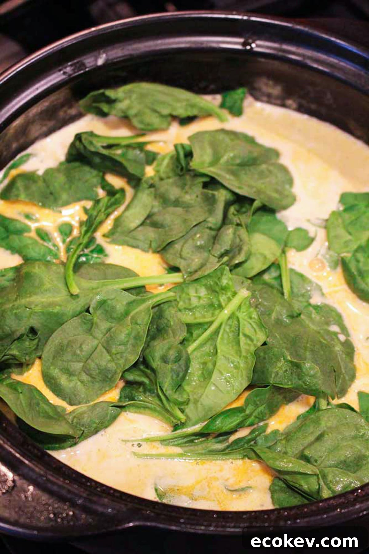 Black pan containing lemon butter cream sauce with fresh spinach.