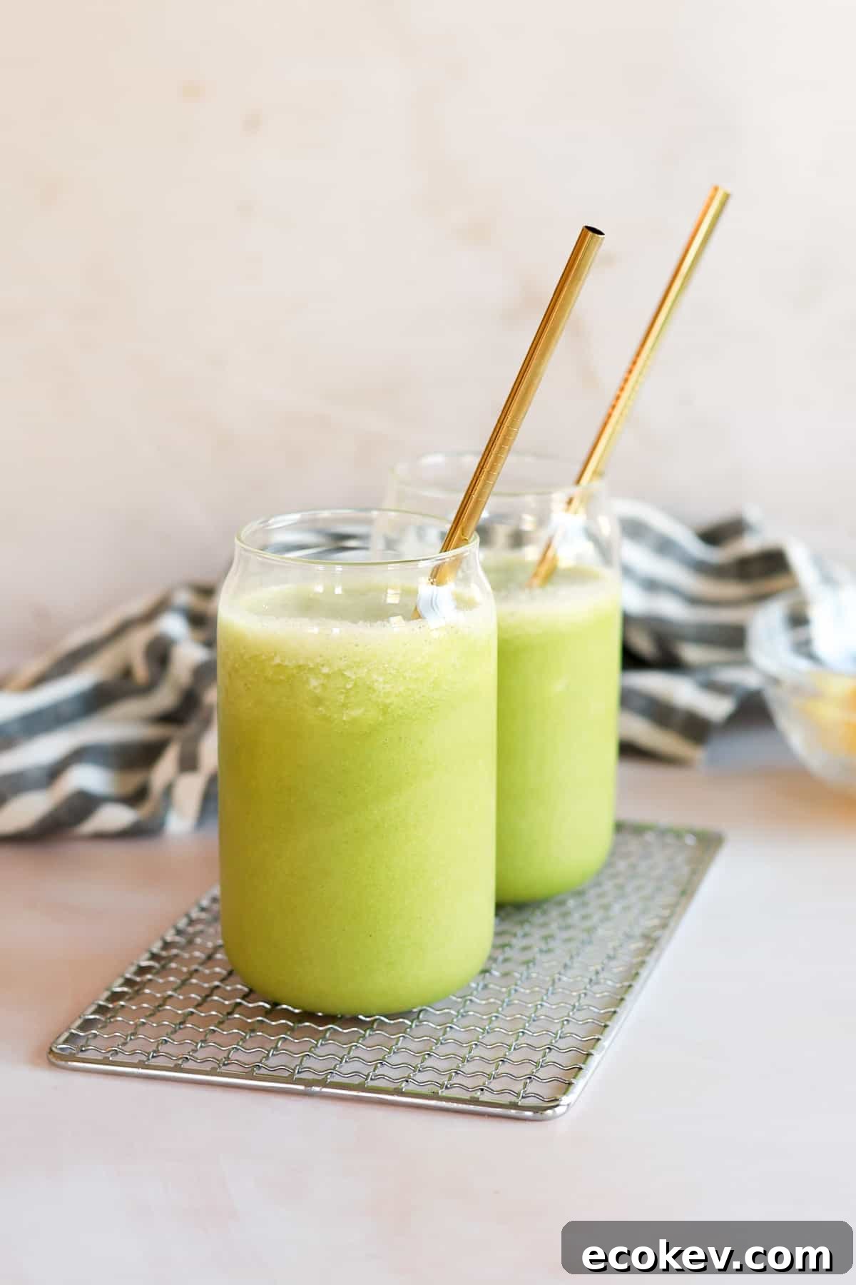 Two kale smoothies in a glass jar with gold metal straws.