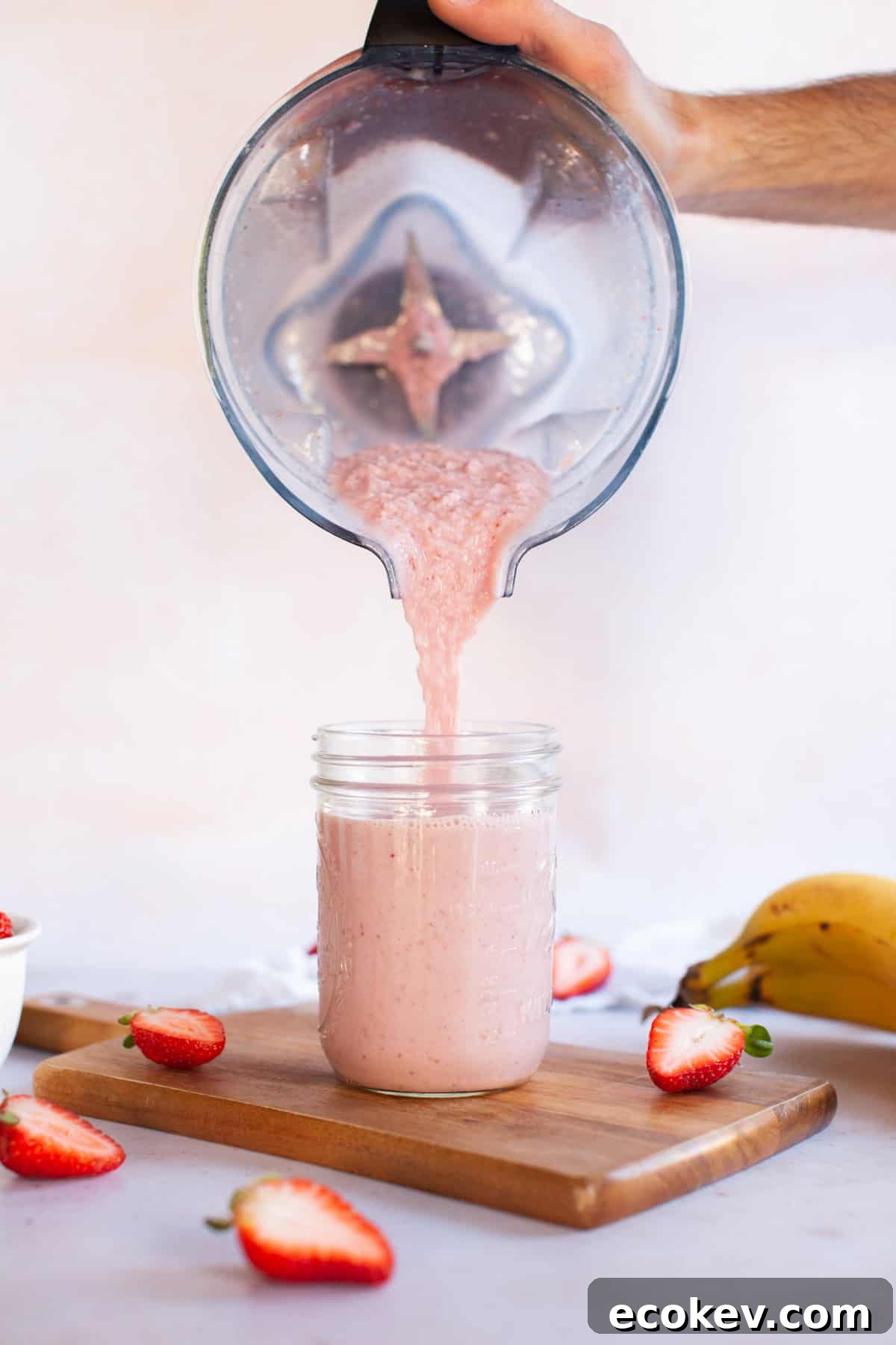 Blender pouring strawberry smoothie into glass jar.