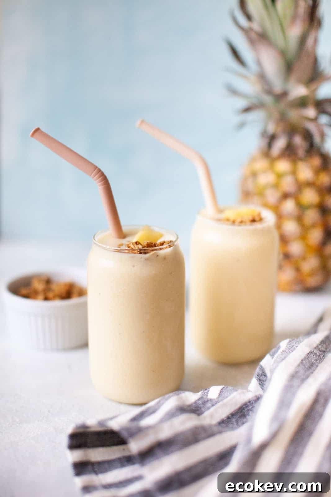 Two pineapple banana smoothies with straws.