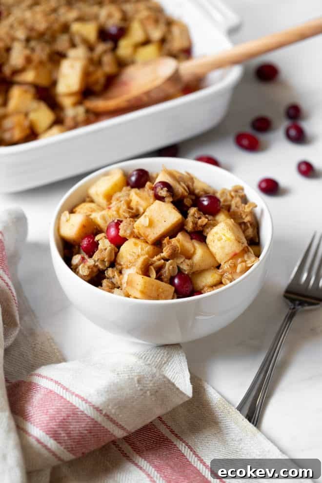 a bowl of apple, pear and cranberry crisp sitting on a table with a fork on the side