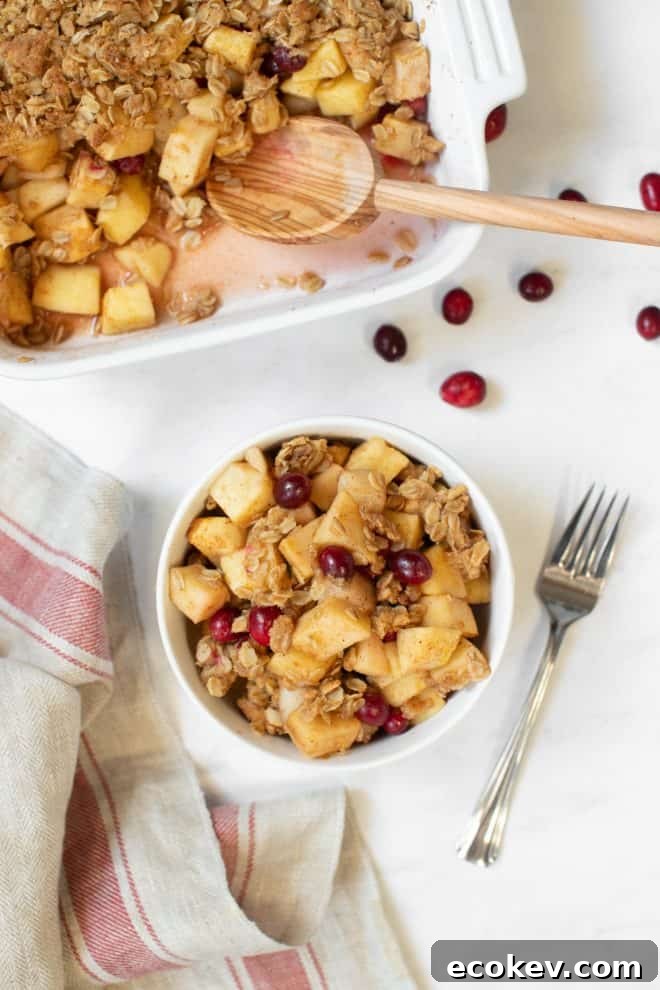 a bowl of apple pear cranberry crisp sitting on a white table with a napkin on the side