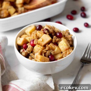 a bowl of apple, pear and cranberry crisp sitting on a table with a fork on the side