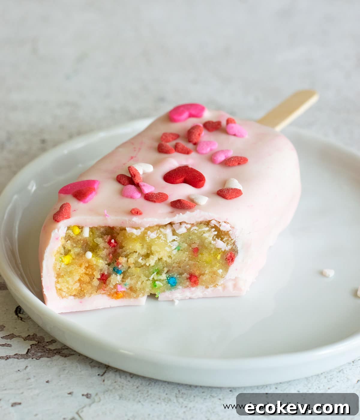 A funfetti cakesicle with a bite removed so you can see the funfetti cake inside.