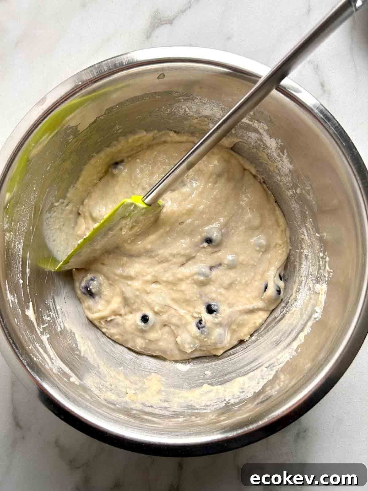 Fluffy Bisquick Muffins Recipe 5 blueberries being folded into batter.